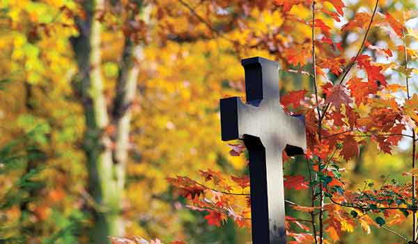 A large cross in a cemetery during the fall season.